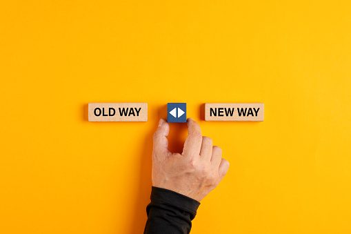 Male hand holds a wooden cube with arrow icon between the options of old way or new way. Deciding to do things in a traditional or a modern fashionable way
